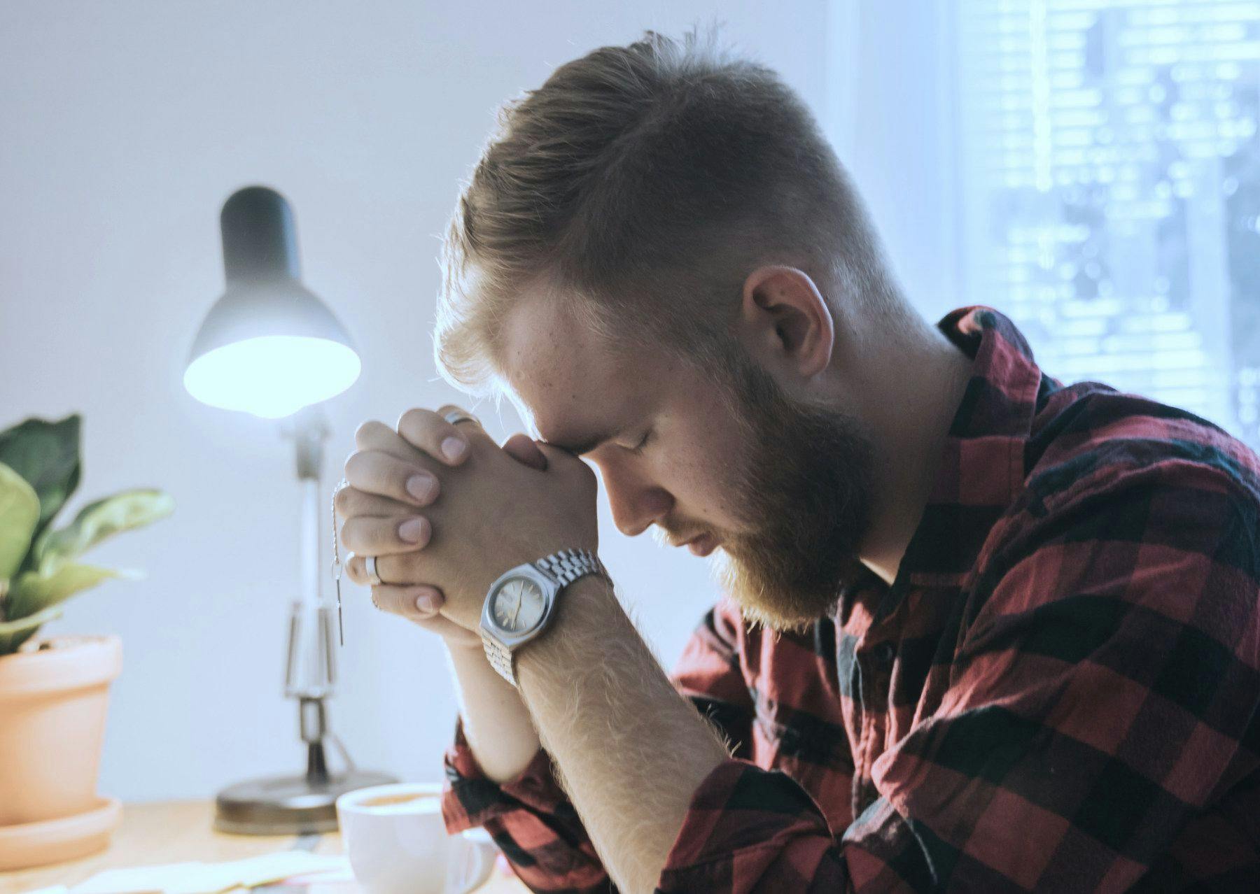 young man praying on desk at home hands clasped